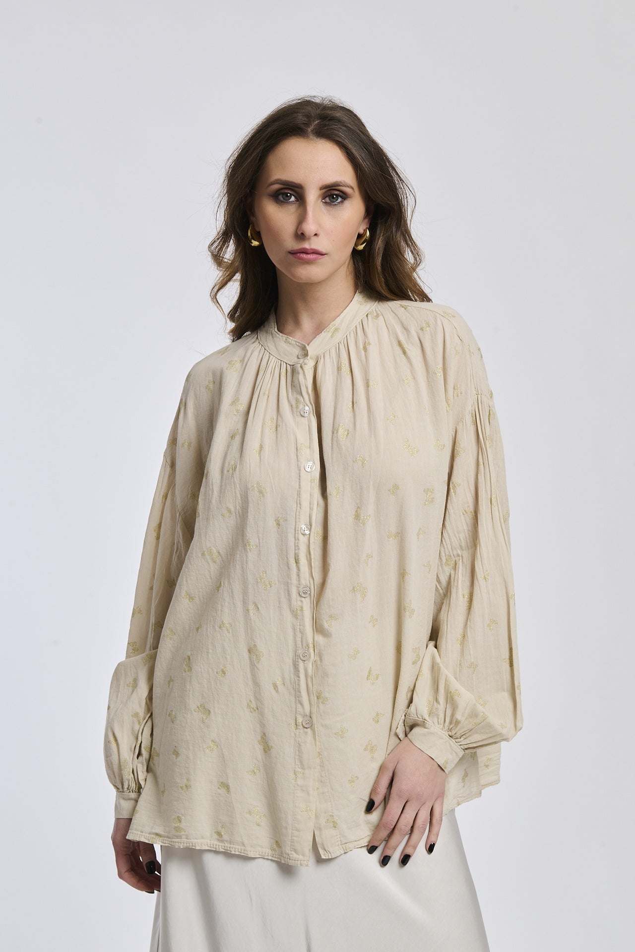 Donna con una camicia beige stampata, maniche a lanterna, collo alto e bottoni centrali, stile bohemien e rassicurante.