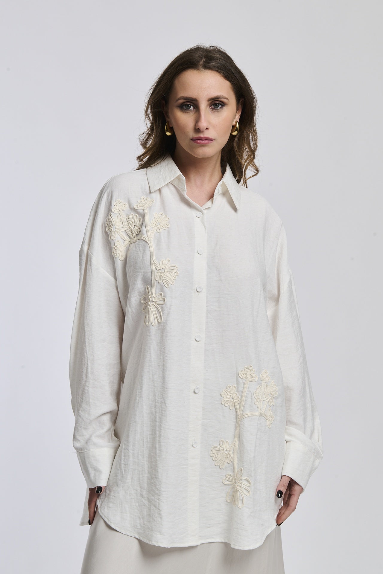 Una donna indossa una camicia di colore blu scuro intenso, con maniche lunghe e un leggero piegamento ai polsi, esprimendo un’aria di serietà e profondità.