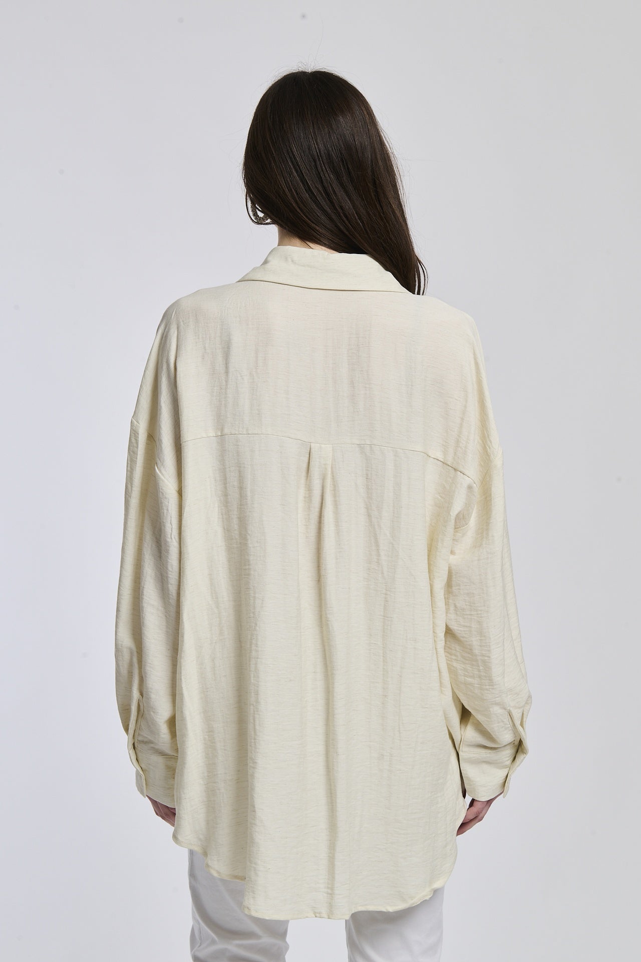 Donna veste una camicia di beige profondo, con colletto a mandarino e bottoni in legno, creando un look di elegante serietà.