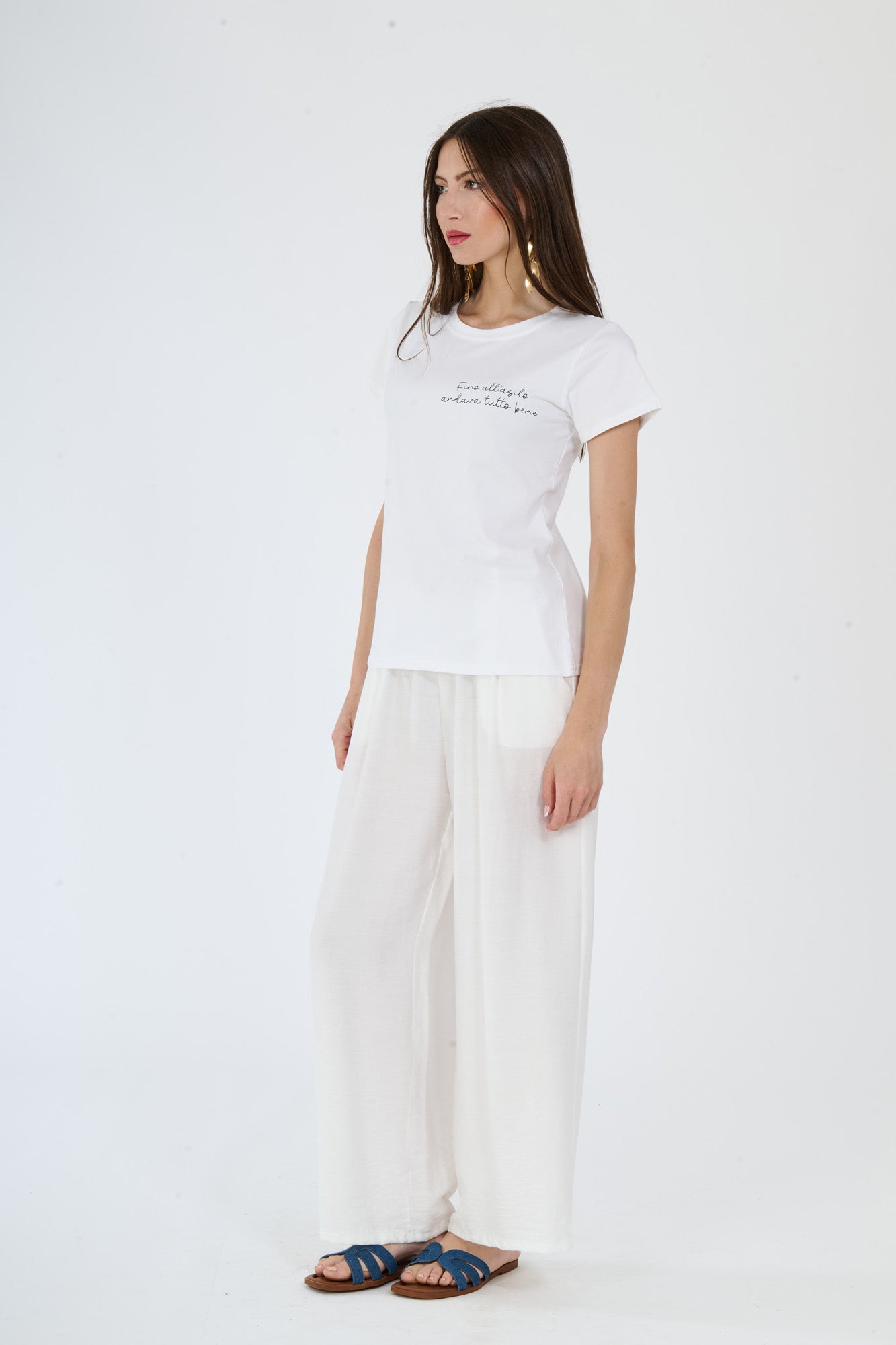 Donna con look bianco: t-shirt decorata e pantaloni ampi, sandali blu
