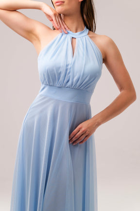 Abito azzurro a halter, donna in posa elegante, pianta verde decorativa accanto
