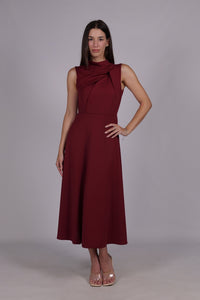 Abito bordeaux da donna, senza maniche, lunghezza midi, dettaglio nodo sul petto, stile elegante e vissuto.