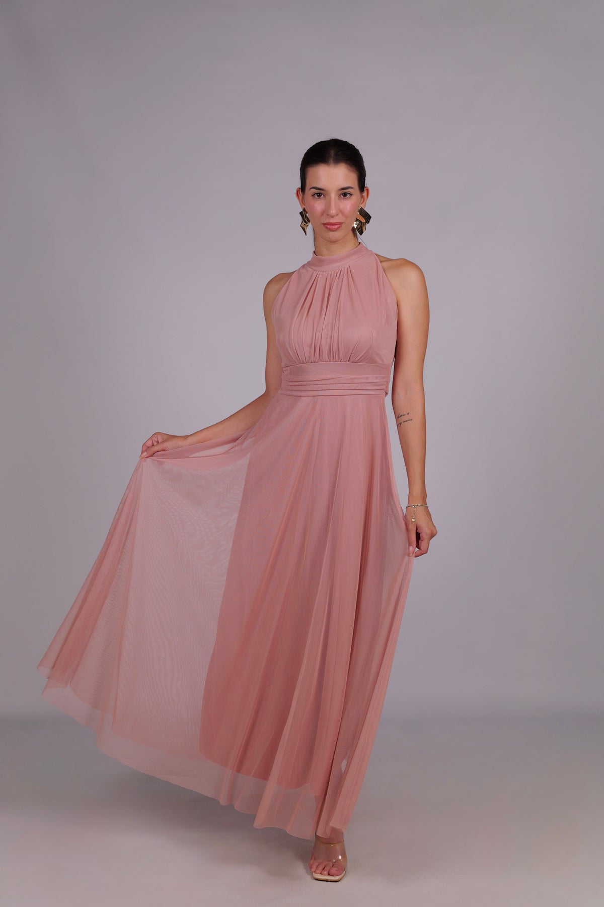 Donna con abito rosa elegante, collo alto a imbarcatura, gonna lunga, foulard in tulle trasparente, look femminile e sofisticato.