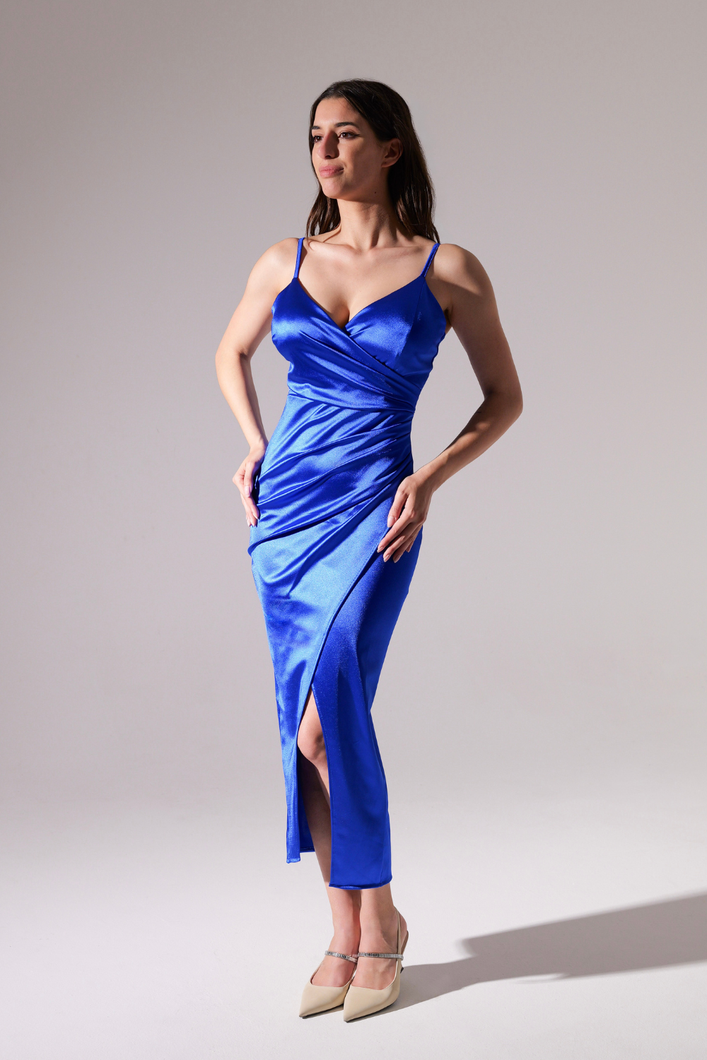 Donna in abito blu scuro satinato, spalline sottili, gonna con aperto laterale, posa elegante