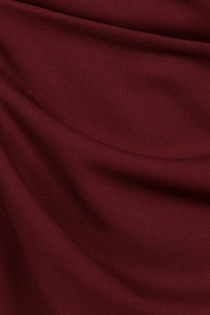 Donna indossa un abito bordeaux senza maniche, lunghezza midi, con nodo al petto, look raffinato.
