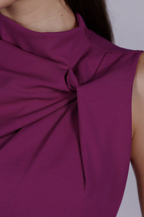 Donna indossa un abito ciliegio senza maniche, lunghezza midi, con nodo al petto, look raffinato.