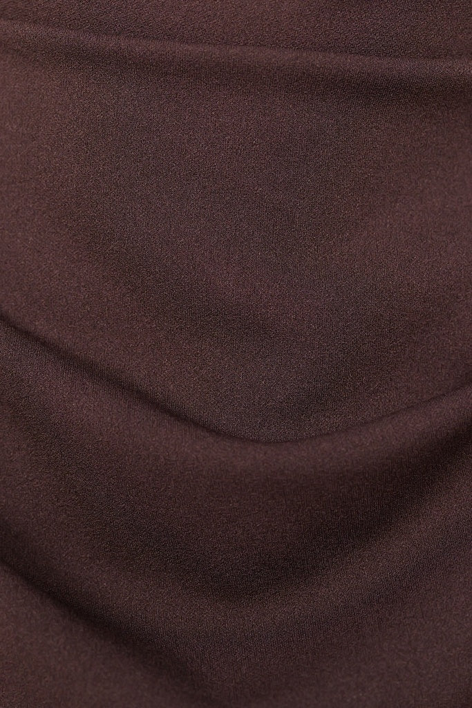 Donna indossa un abito marrone senza maniche, lunghezza midi, con nodo al petto, look elegante.