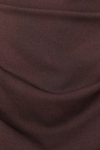 Donna indossa un abito marrone senza maniche, lunghezza midi, con nodo al petto, look elegante.