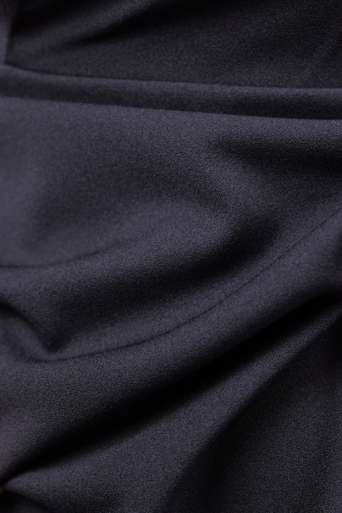 Donna indossa un abito nero senza maniche, lunghezza midi, con nodo al petto, look elegante.