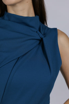 Donna indossa un abito ottanio senza maniche, lunghezza midi, con un nodo sul petto, look sofisticato.