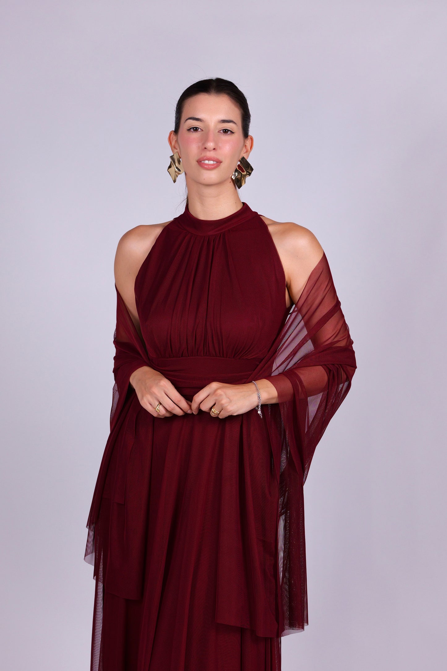 Donna indossa un abito vino elegante, collo a imbarcatura, gonna lunga, con foulard in tulle trasparente, look raffinato.
