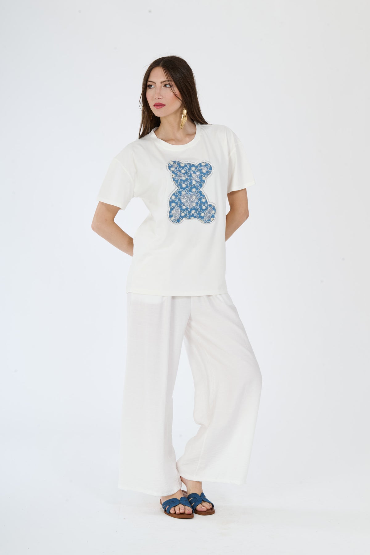 Donna indossa un completo bianco con t-shirt e pantaloni, abbinato a sandali blu