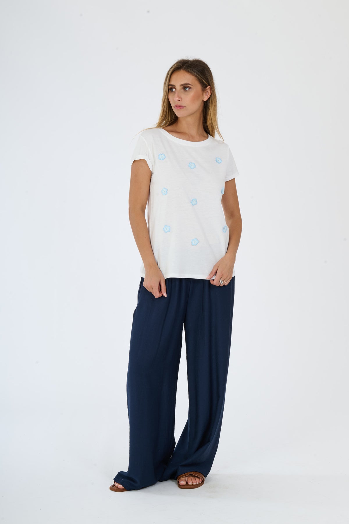 Donna indossa una maglietta bianca a maniche corte con pois azzurri e pantaloni larghi scuri, presentazione di un outfit casual e minimalista