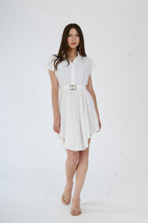 Vestito bianco a camicia con taglio asimmetrico e bottoni metallici, ideale per un look moderno ed affascinante.