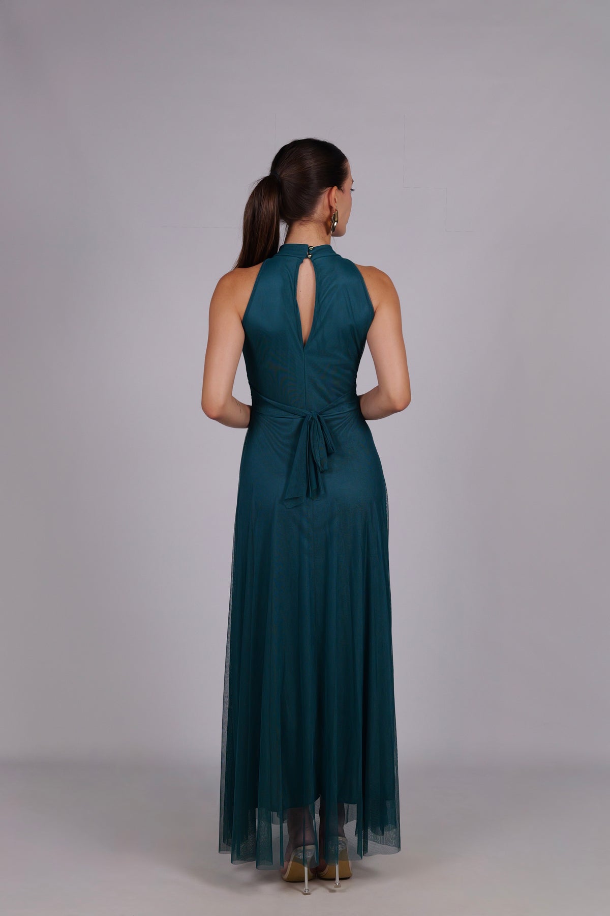 Modella con abito ottanio a gonna lunga, collo a imbarcatura, foulard in tulle trasparente, outfit elegante per occasioni formali.