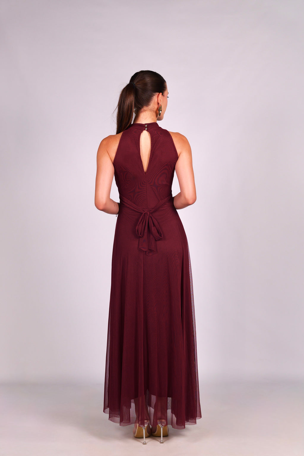 	Modella con abito vino a gonna lunga, collo a imbarcatura, foulard in tulle trasparente, outfit elegante per serate speciali.
