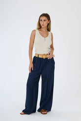 Outfit con top beige senza maniche e pantaloni larghi bianchi, accessorizzato con una cintura in pelle, stile casual e raffinato.