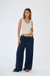 Outfit con top beige senza maniche e pantaloni larghi bianchi, accessorizzato con una cintura in pelle, stile casual e raffinato.