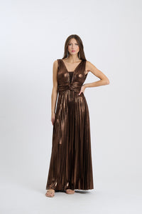Una donna indossa un abito da sera lungo senza maniche di colore marrone con plissé e scollatura a V, su sfondo chiaro.