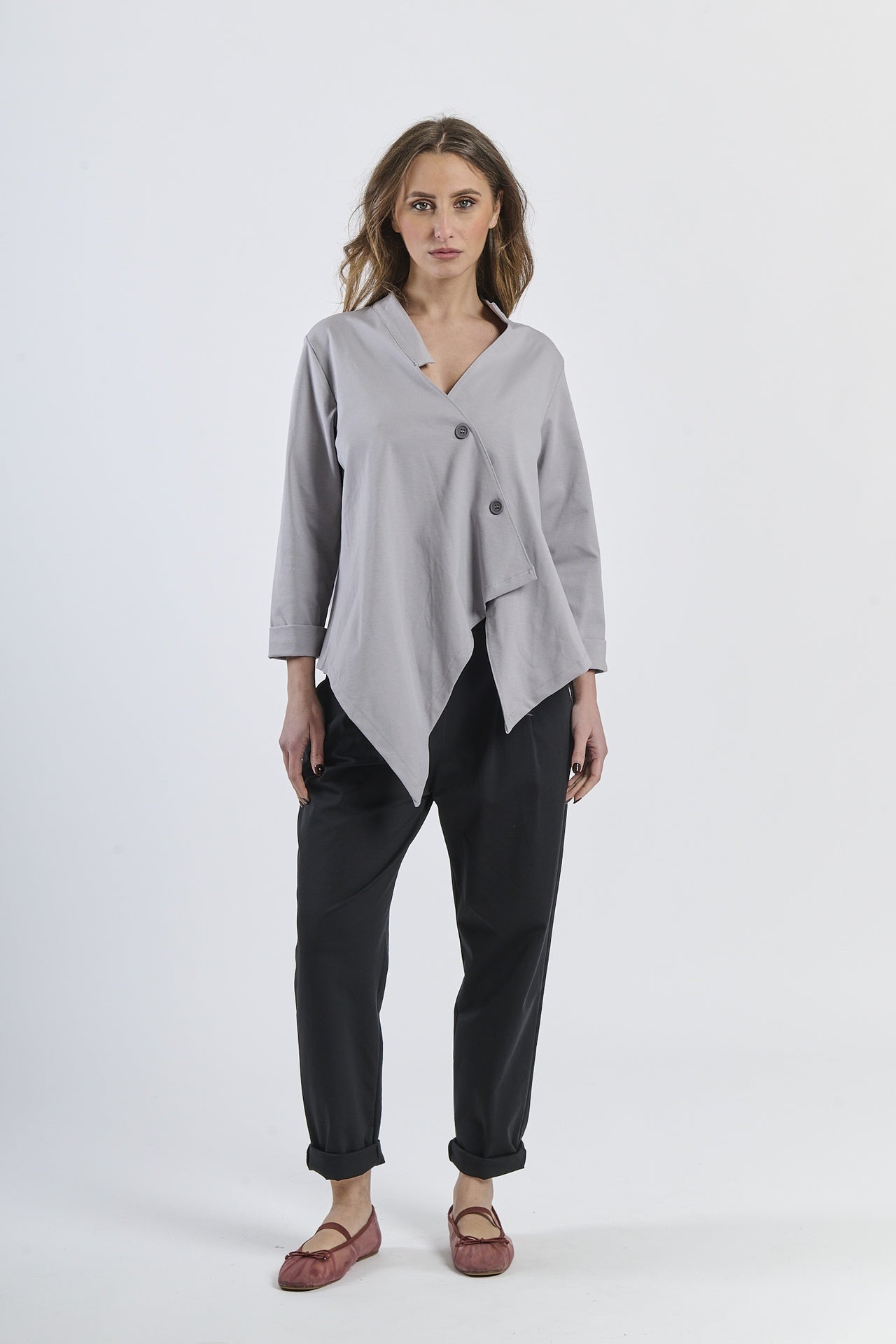 Outfit di camicia grigio irregolare, pantaloni beige avvolgenti e mocassini scuri, eleganza sobria