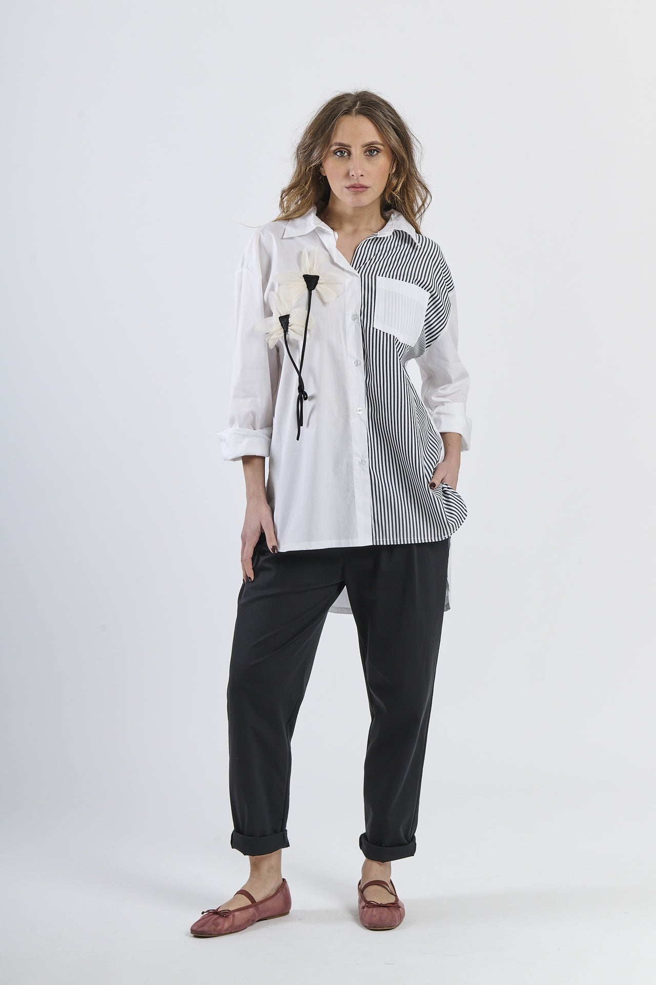 Camicia  nero oversize bicolor bianca e rosa a righe, con fiore decorativo e tasca contrastante, abbinata a pantaloni scuri e mocassini rossi