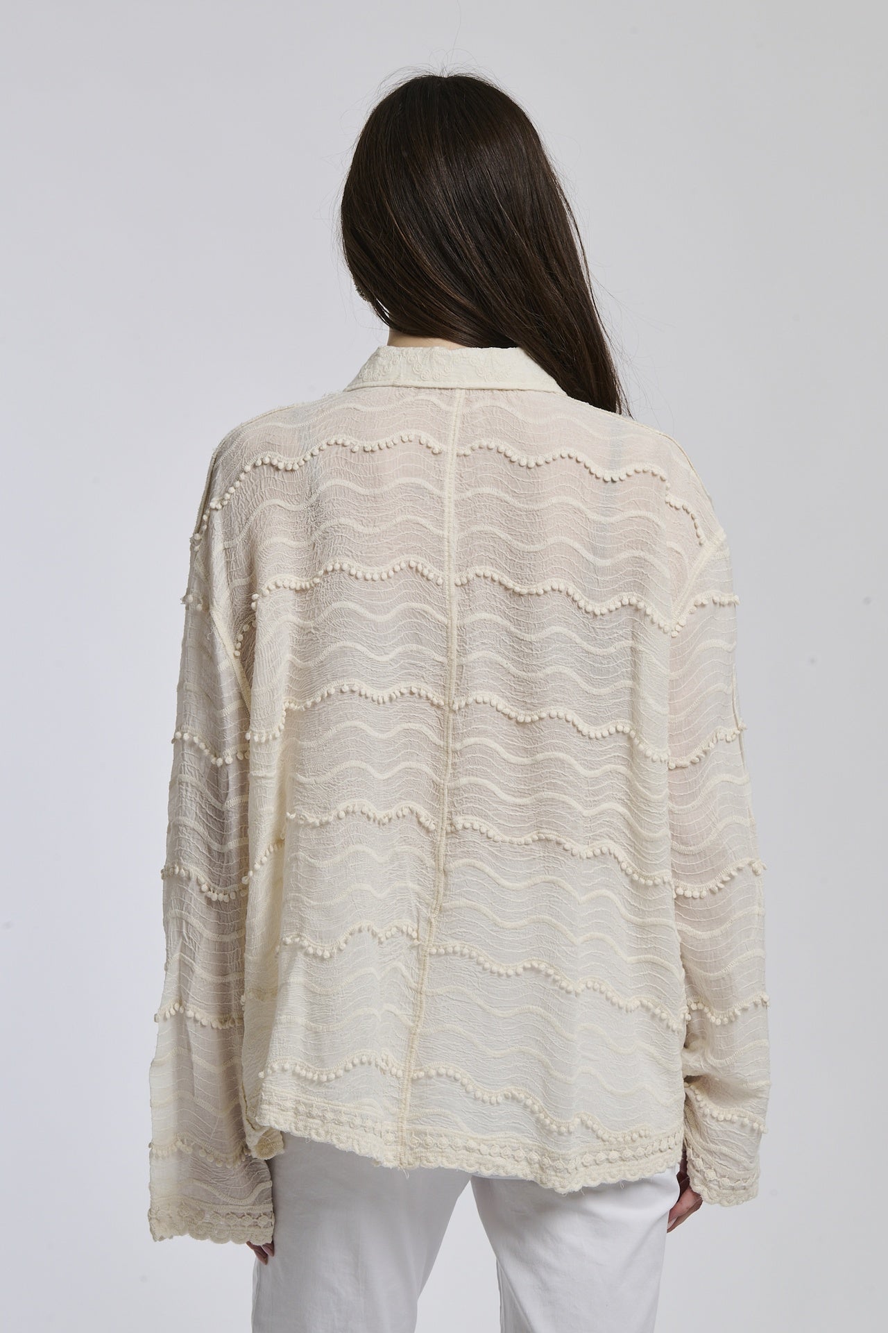 Camicia a maniche lunghe beige con texture ricamata, abbinata a pantaloni bianchi, sfondo bianco