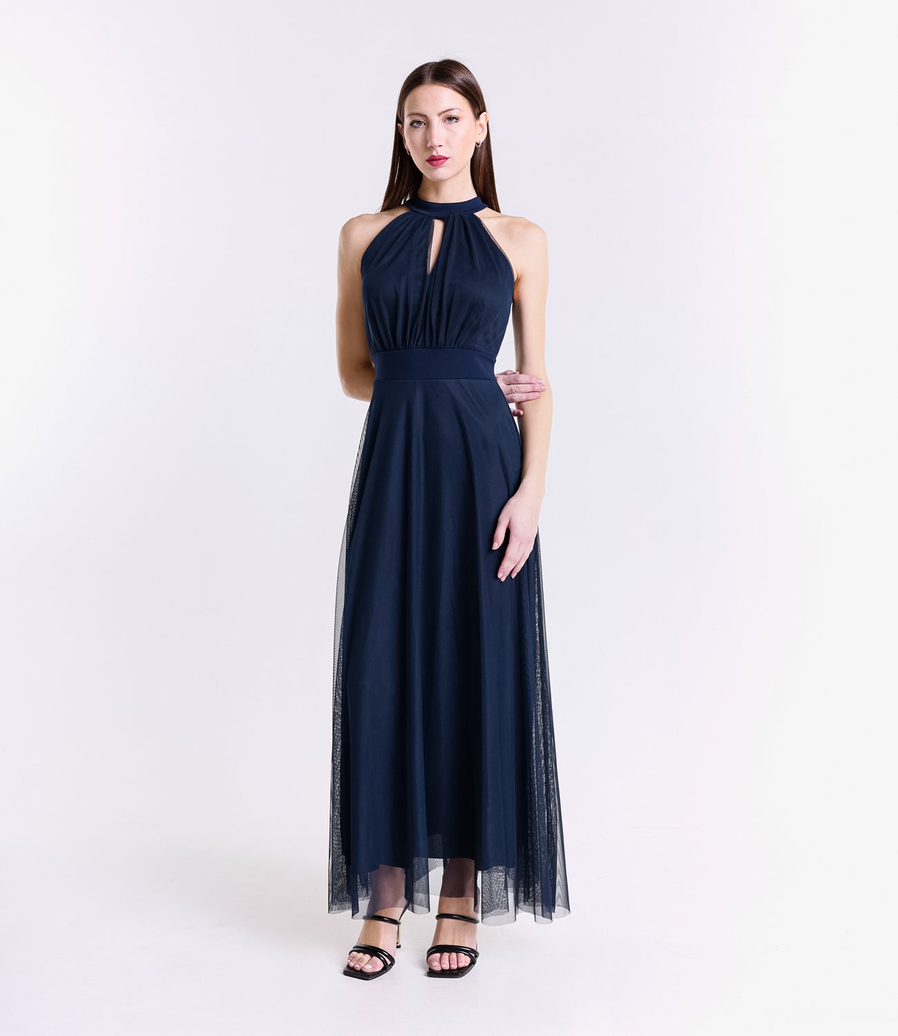 Donna con abito lungo blu scuro, colletto a nodo, pianta verde tropicale accanto