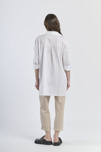 Outfit casual con camicia a righe navy asimmetrica, dettaglio floreale e pantaloni marroni, scarpe mocassini rame