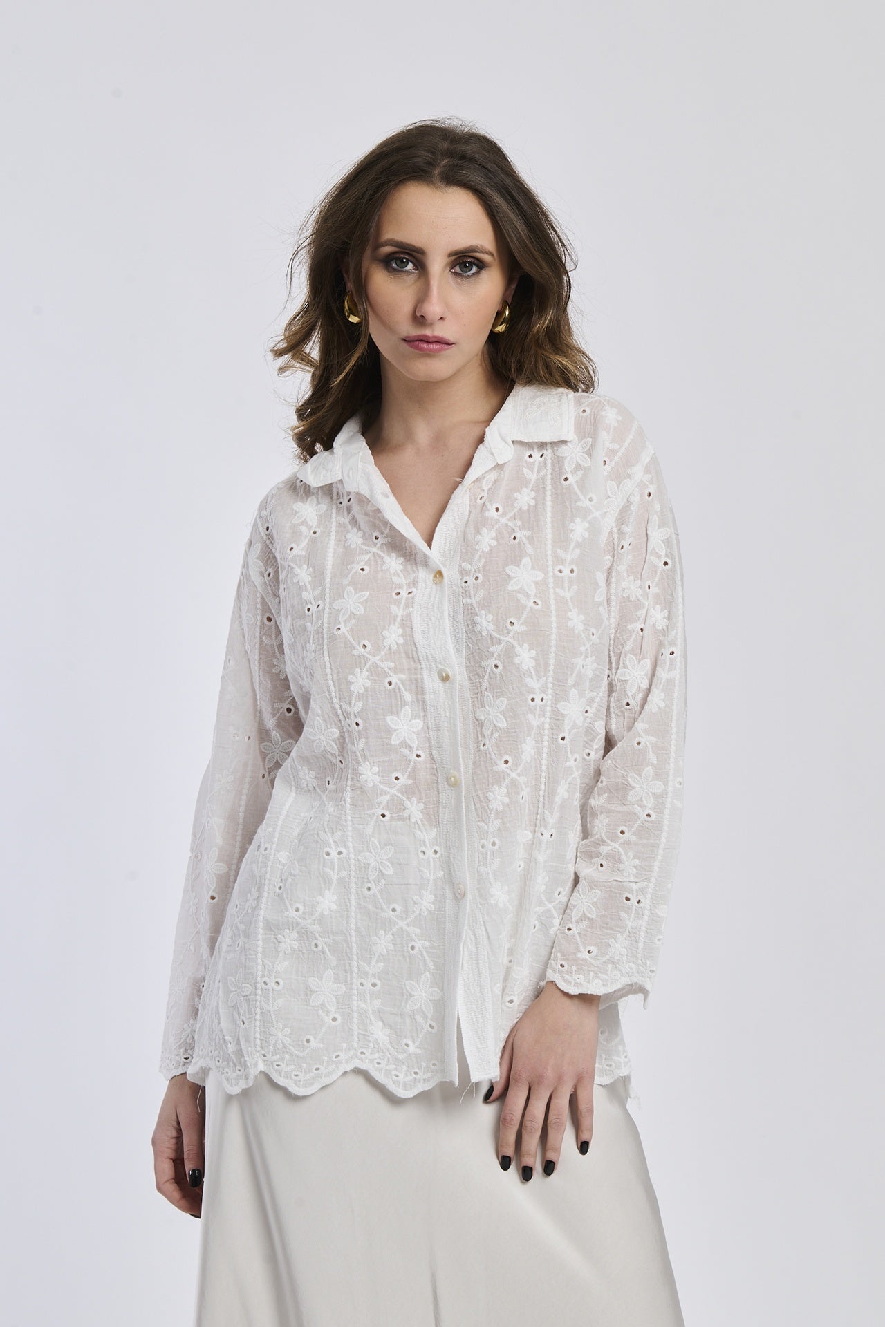 Donna con camicia bianca ricamata, colletto a bottone e orecchini dorati, sfondo bianco