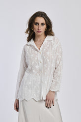 Donna con camicia bianca ricamata, colletto a bottone e orecchini dorati, sfondo bianco