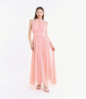 Donna con abito lungo rosa, colletto a nodo, pianta verde tropicale accanto