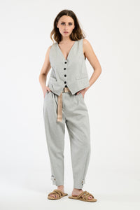 Modella indossa completo grigio: gilet senza maniche e pantaloni, stile sobrio e moderno.