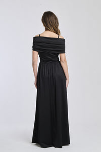 Abito nero a spalline scollate, tessuto lustrato, fascia in vita che accentua la silhouette.