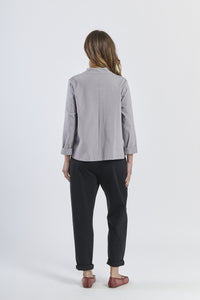Combinazione di camicia grigio con apertura asimmetrica, pantaloni beige chiari e scarpe marroni, modernità minimal