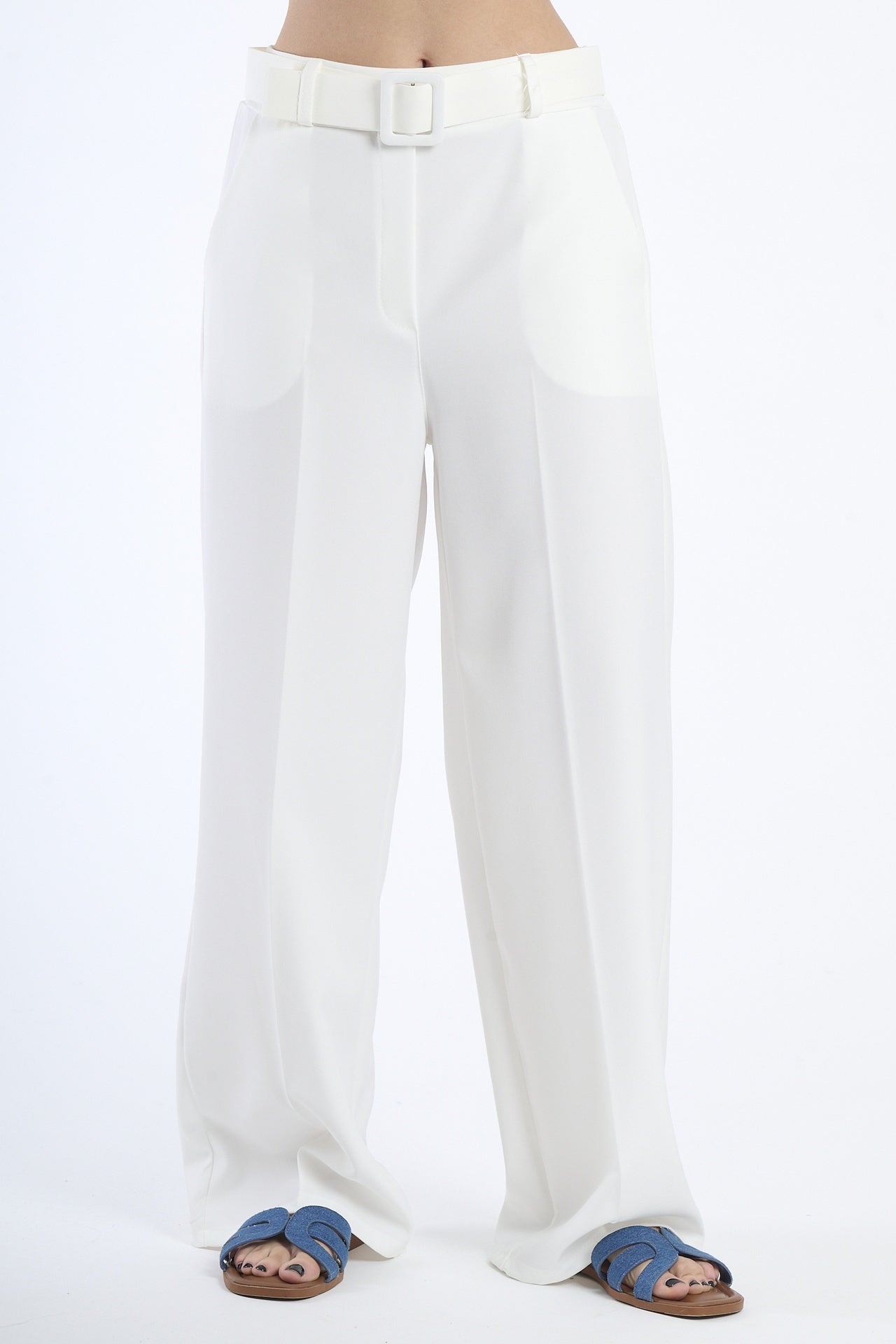 Pantaloni larghi bianchi con cintura, taglio a zampa, abbinati a sandali.