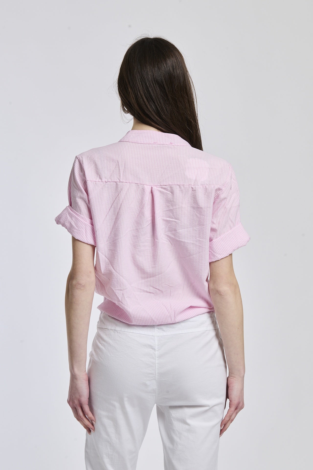 Donna con camicia a righe rosa, maniche lunghe e nodo laterale, ideale per un look romantico.