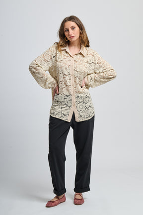 Camicetta beige con motivi, collo camiciera e maniche lunghe, abbinata a pantaloni neri.