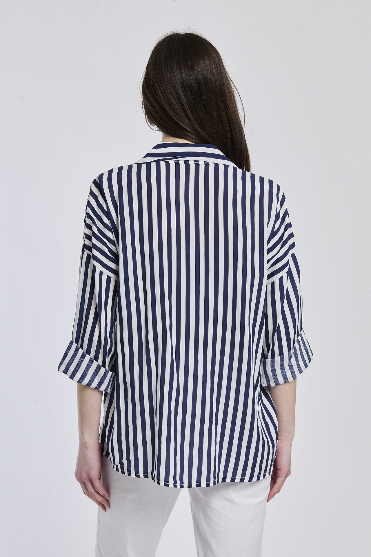 Donna indossa una camicia a righe navy, maniche lunghe e tasca decorativa, stile preppy e raffinato.