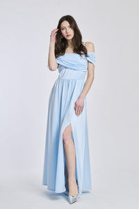 Donna indossa un abito lungo azzurro, spalline scollate, fascia in vita e apertura laterale elegante.