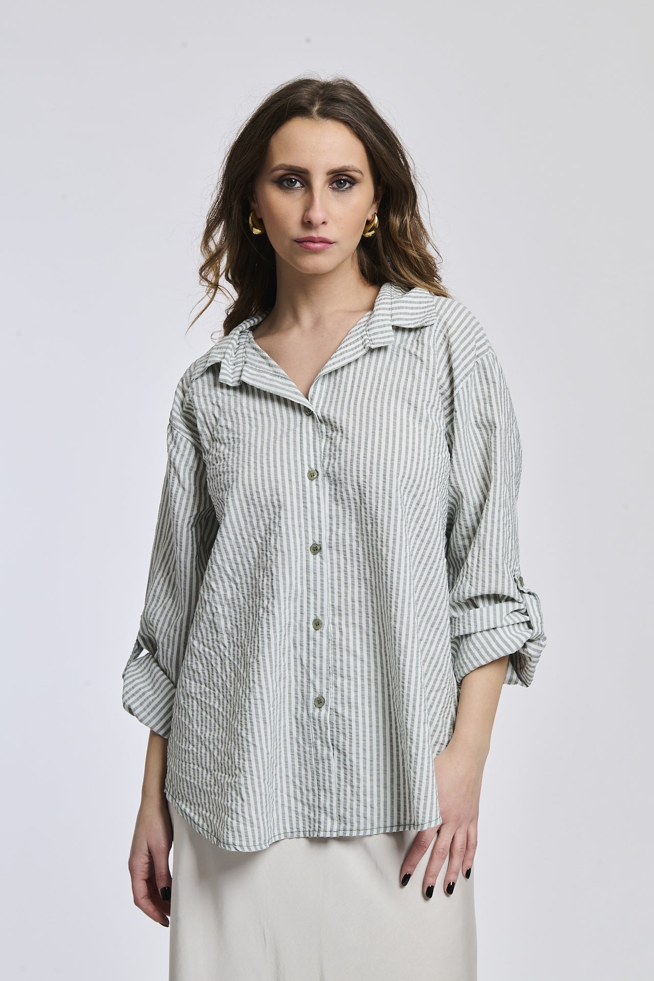 Donna indossa una camicia a righe militares, oversize, colletto a camicia, bottoni frontali e maniche arrotolate.