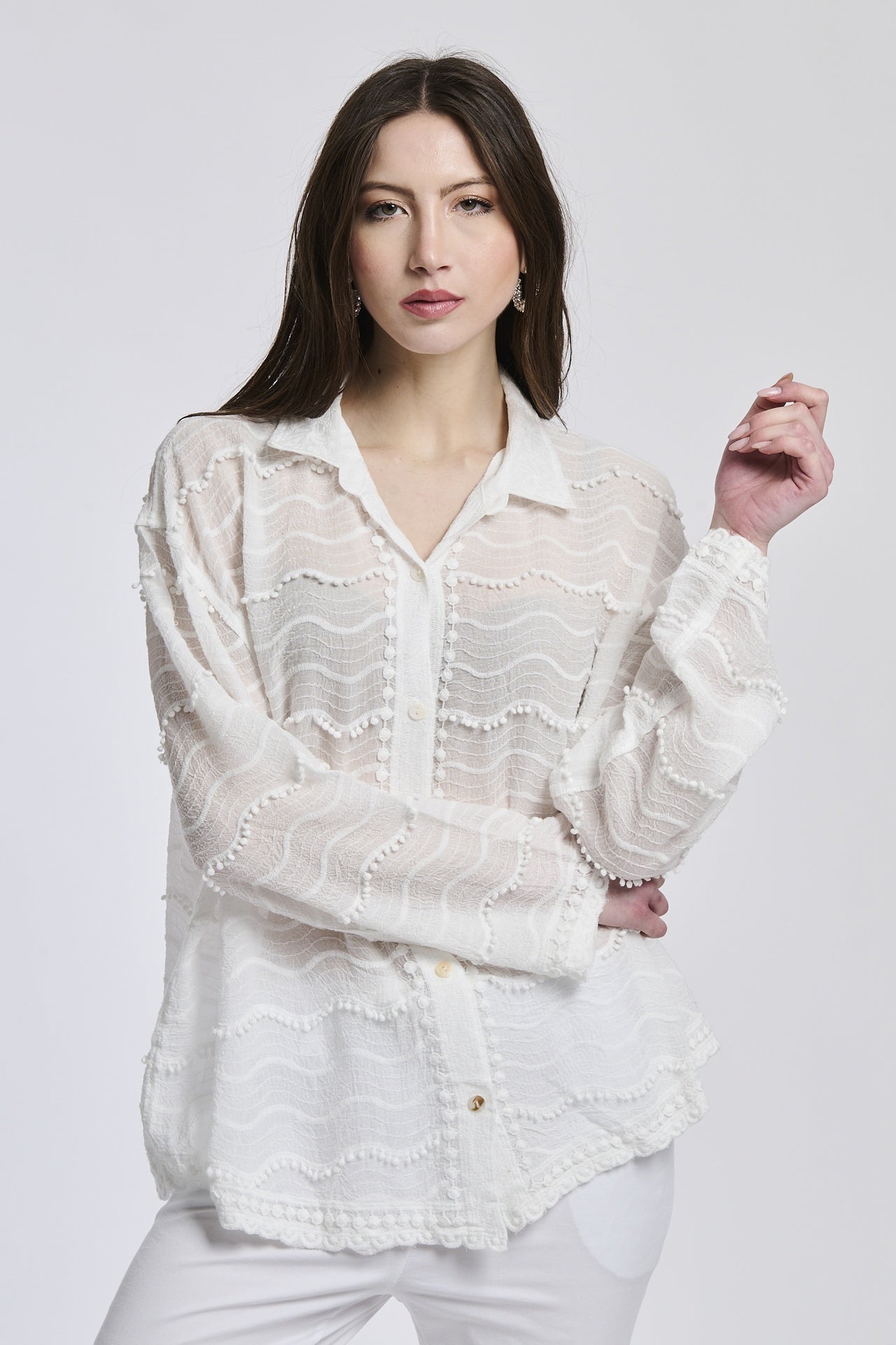 Donna con camicia oversize in pizzo bianco e pantaloni bianchi, posa con mani sulle fianche