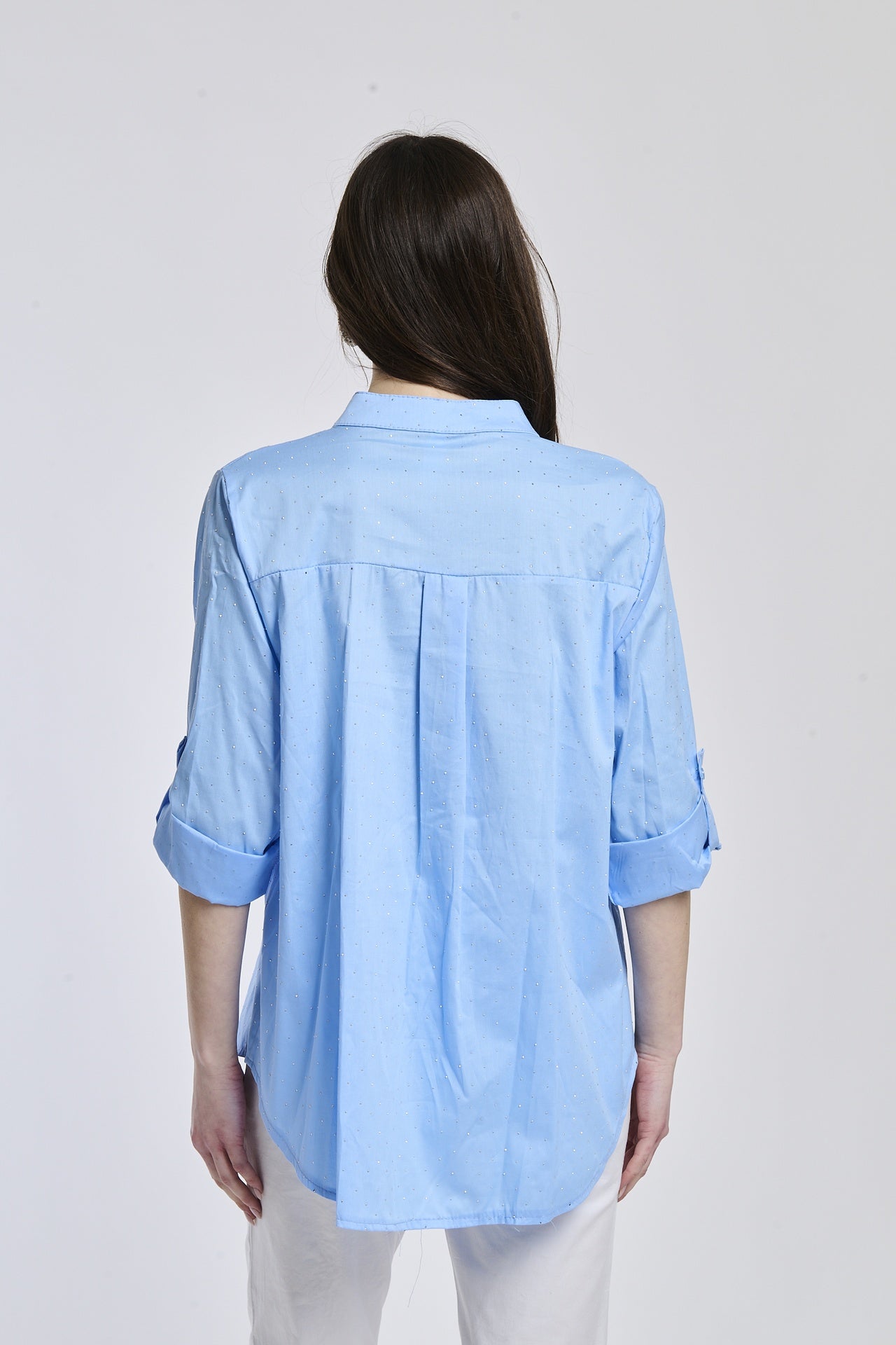 Donna indossa una camicia azzurra oversize, colletto coreano, bottoni frontali e maniche arrotolate a 3/4.