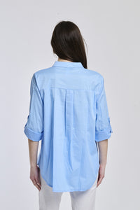 Donna indossa una camicia azzurra oversize, colletto coreano, bottoni frontali e maniche arrotolate a 3/4.
