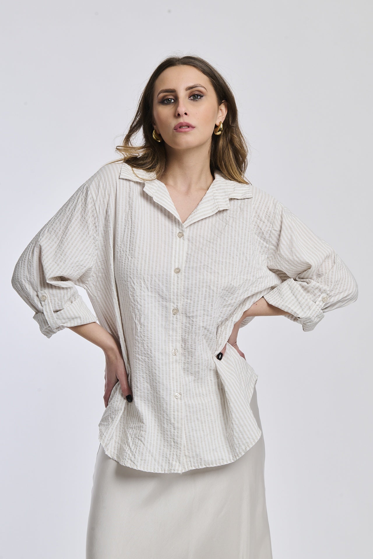 Camicia oversize beige a righe, colletto a V sfiorato, bottoni frontali e maniche arrotolate, perfetta per l’uso quotidiano.