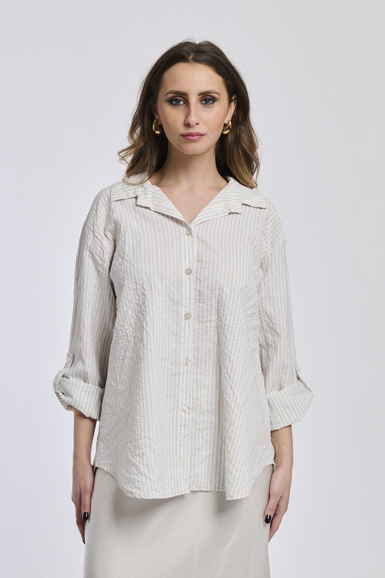 Donna con camicia a righe beige, oversize, colletto a camicia, bottoni frontali e maniche arrotolate.