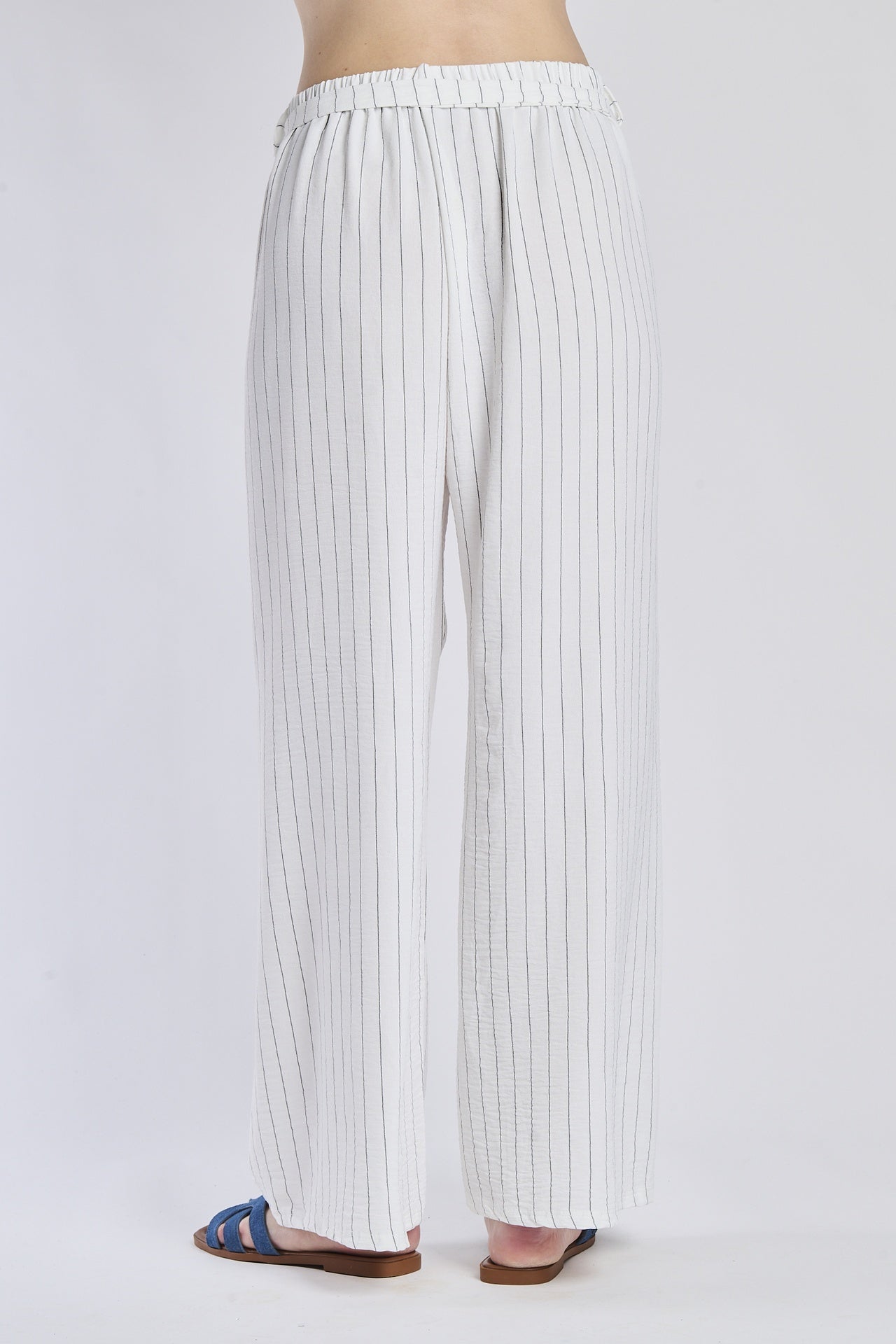 Pantaloni larghi bianchi con coulisse e nodo in vita, abbinati a sandali.