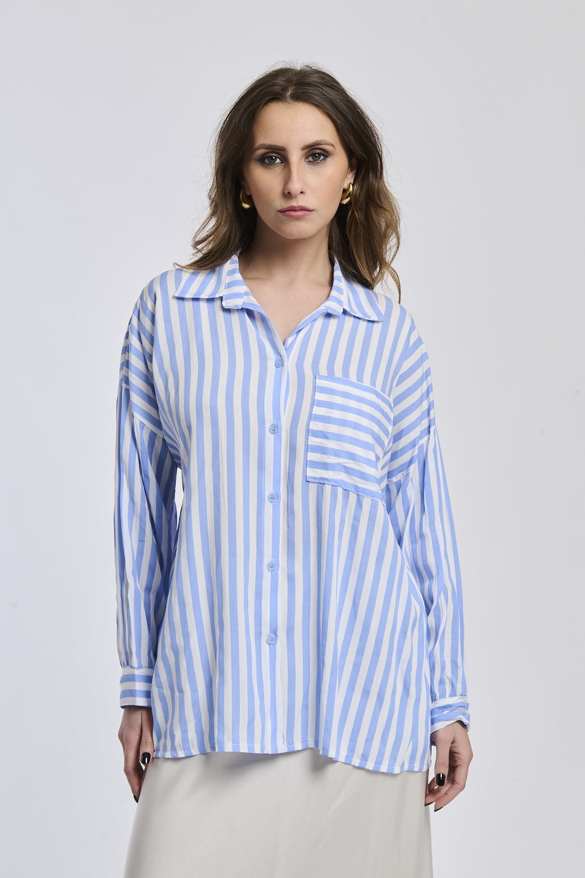 Donna indossa una camicia a righe azzurre e bianche, con colletto e tasca sul petto, stile casual e moderno.