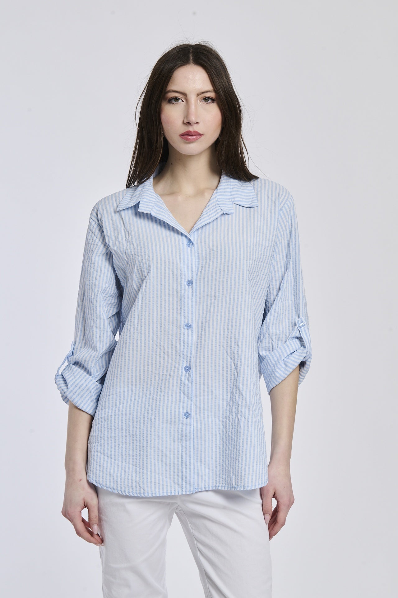 Camicia oversize azzurra a righe, colletto a V sfiorato, bottoni frontali e maniche arrotolate, idea per outfit quotidiano.
