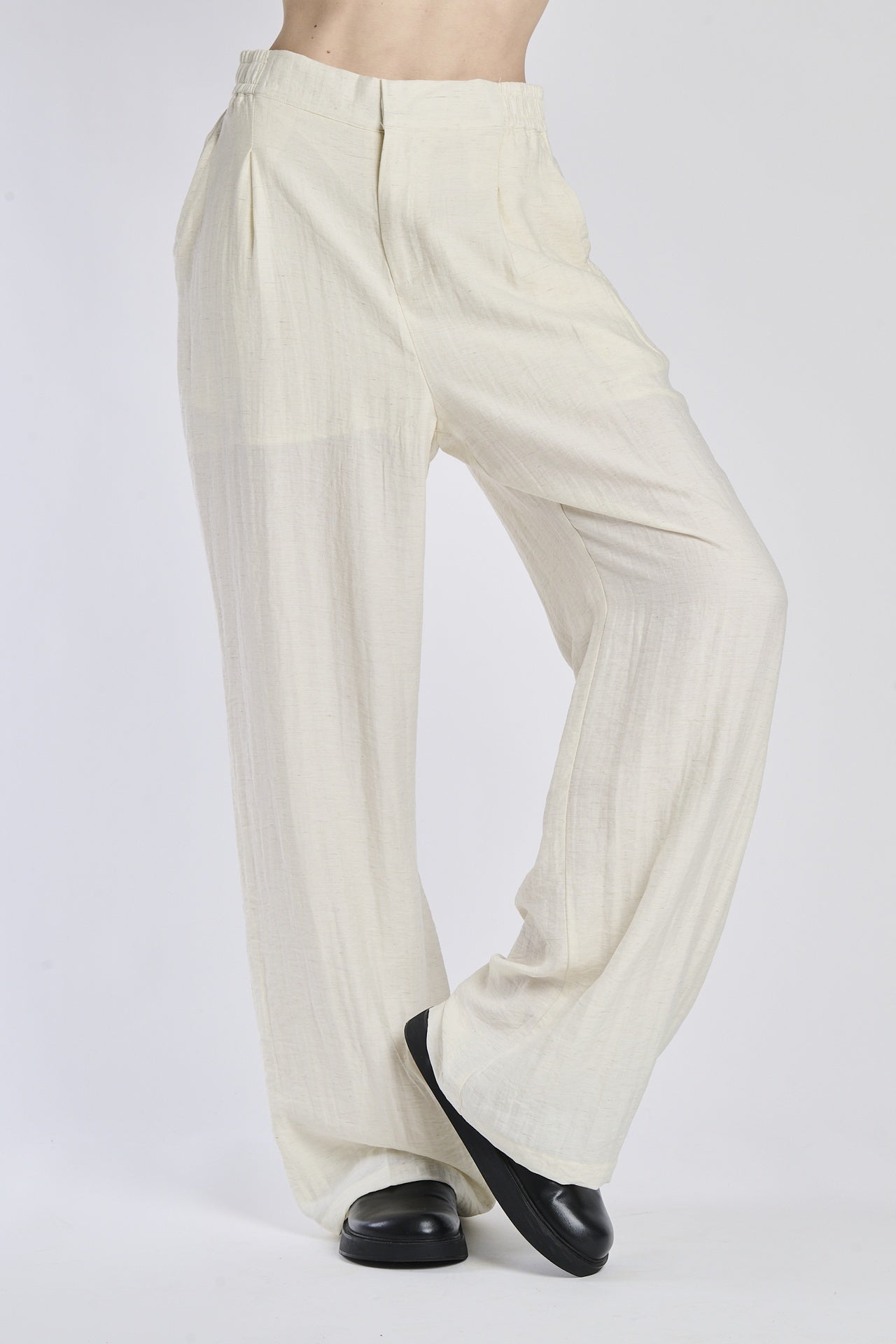 Pantaloni larghi bianchi, tessuto leggero, vita alta e ampie gamba, abbinati a mocassini neri.