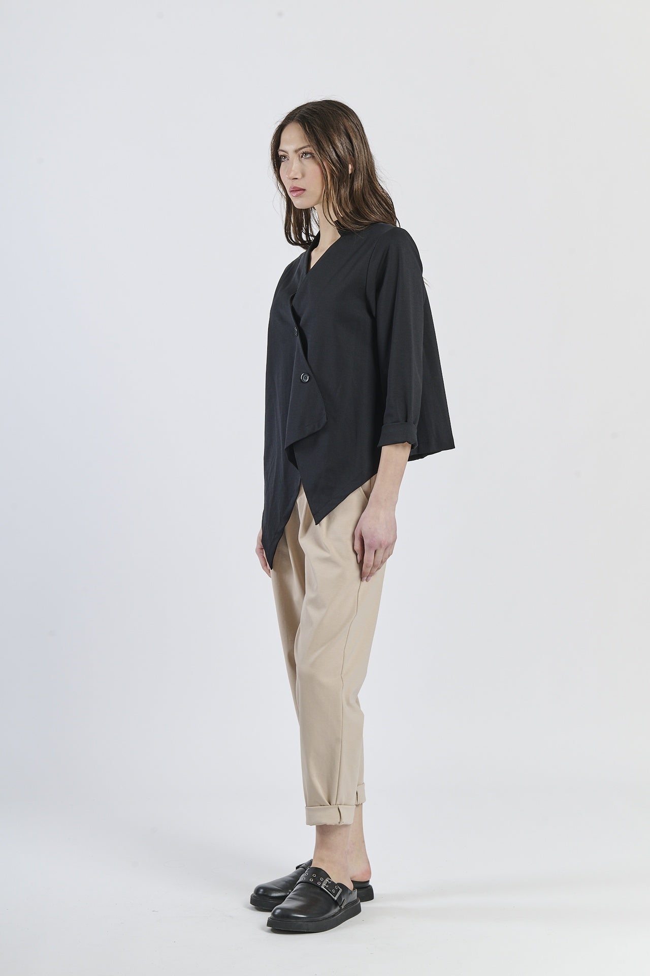 Look con camicia nero a taglio asimmetrico, pantaloni beige a gamba larga e mocassini marroni